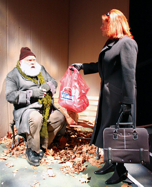 A bearded man in a winter coat and hat sits on a bench covered in autumn leaves, looking surprised as a woman in a long coat and gloves hands him a red plastic bag while holding a briefcase.