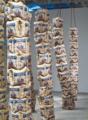 Several tall, vertical stacks of burlap sacks labeled Castillo hang from the ceiling on thick ropes in a modern art gallery space with concrete floors.