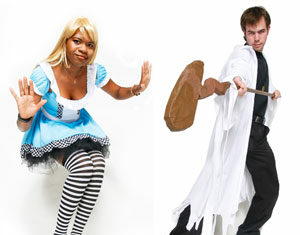 Two people in costume: one wearing a blonde wig, blue dress, and striped stockings; the other in a white robe holding a large prop weapon, both posing against a white background.
