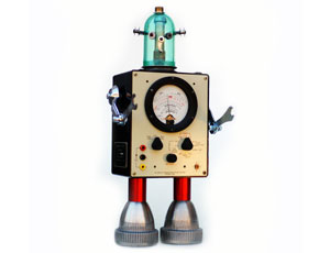 A toy robot made from various electronic parts, featuring a square body with a gauge meter, metal arms, red legs, and a blue glass dome head with a small bulb on top, standing against a white background.