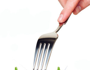 A hand holding a fork above a large, bright green grasshopper, as if about to eat it, against a white background.
