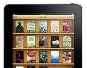 An iPad displaying a digital bookshelf with various book covers on its screen, showing multiple rows of eBooks in the iBooks app.