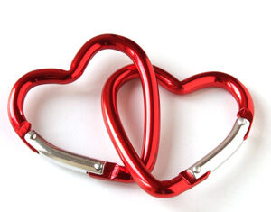 Two red, heart-shaped carabiners are interlocked and lying on a white background.
