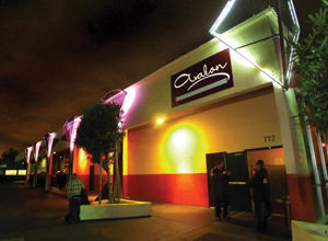 Nighttime view of the exterior of Avalon nightclub, featuring a red and white facade, illuminated by purple and yellow lights, with a few people standing near the entrance under a sign reading Avalon.