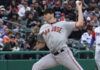 A baseball pitcher in a gray San Jose uniform prepares to throw a pitch during a game, with spectators watching from the stadium seats in the background.