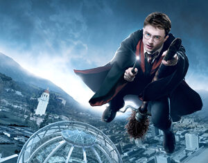 A young man in glasses and a black robe flies on a broomstick over a modern cityscape, with a large glass-domed building below and mountains in the background.