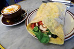 A plate with a veggie-filled wrap next to a cup of cappuccino with foam and cinnamon, set on a gray table.