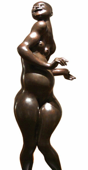 A bronze sculpture of a nude woman with a curvy body standing on tiptoe, her arms bent and hands gesturing gracefully, with a joyful expression on her face.