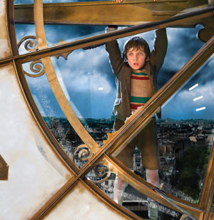 A young boy in old-fashioned clothes hangs from the hands of a large clock tower, with a cityscape visible in the background under a cloudy sky.