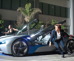 A man and woman in business attire crouch beside a futuristic car with open gull-wing doors, appearing alert and ready for action outside a modern building at night.