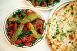 A bowl of okra and tomato curry garnished with fresh cilantro, served alongside a piece of naan bread sprinkled with chopped herbs.