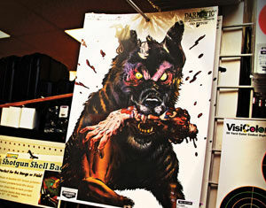 A poster of a menacing, bloodied zombie wolf with glowing eyes and a severed arm in its mouth is displayed on a store rack.