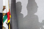 A California state flag next to a curtain showing the shadows of two people in profile, suggesting a behind-the-scenes or private conversation.