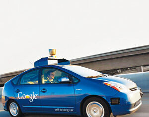 A blue car labeled Google self-driving car with sensors on the roof is driving on a highway, with a blurred background indicating motion.