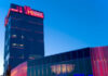 A modern building with a tall tower and a glass-fronted section, both illuminated with pink and blue lights at dusk. The sign on the tower reads CASINO MATRIX.