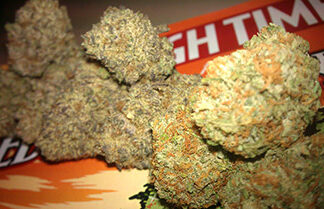 Close-up of several cannabis buds placed on top of a colorful magazine cover that reads HIGH TIMES in bold letters. The buds have a dense, textured appearance with green and orange hues.