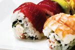 Close-up of assorted sushi rolls on a white plate, including pieces topped with slices of tuna and shrimp, with visible rice, seaweed, and other fillings.