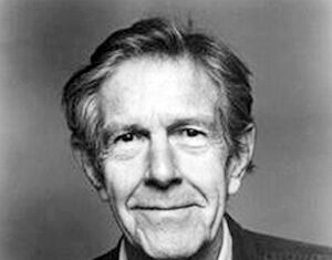 Black and white portrait of an older man with light hair, wearing a collared shirt and jacket, looking at the camera and smiling slightly against a plain background.