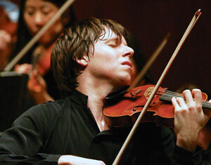 A violinist in a black shirt plays the violin passionately with eyes closed, surrounded by other orchestra musicians in the background.