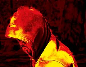A person wearing a hooded sweatshirt sits or stands with their head bowed. The image is heavily filtered in intense red and yellow tones, creating a dramatic and abstract effect.
