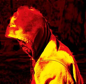 A person wearing a hooded sweatshirt sits or stands with their head bowed. The image is heavily filtered in intense red and yellow tones, creating a dramatic and abstract effect.
