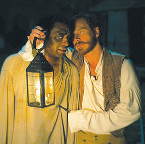 A man in a light shirt holds a lantern near another man’s face at night, while gripping his shoulder and pressing a knife against his chest, creating a tense and dramatic atmosphere.