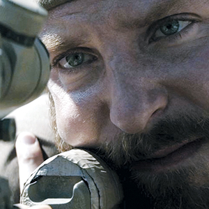 A close-up of a man aiming through a sniper rifle scope, showing intense focus in his eyes and rugged facial features, with his face partially resting against the rifle.