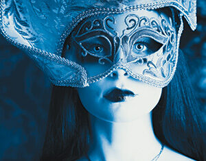 A woman wearing an ornate mask and elaborate costume gazes forward. Her lips are painted dark, and she wears a decorative necklace. The image is tinted blue, enhancing the dramatic, mysterious atmosphere.