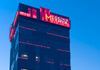 A tall building with red neon signage reading Matrix on the rooftop, illuminated against a clear blue evening sky.