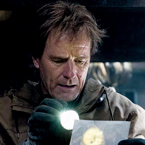 A man wearing gloves holds a flashlight and examines a piece of paper intently in a dimly lit setting.