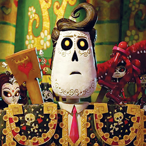 Animated character with a white skull-like face, large black eyes, and stylized hair wears a decorated suit with skull motifs. Colorful, ornate background and other similarly styled characters are visible behind him.