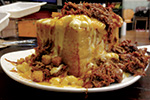 A plate piled high with shredded meat, melted cheese, and sauce covering a large serving of cornbread or casserole, creating a hearty and indulgent meal.