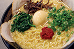 A bowl of ramen with yellow noodles, sliced pork, green onions, spinach, a soft-boiled egg, wood ear mushrooms, and a dollop of red chili paste in rich broth.