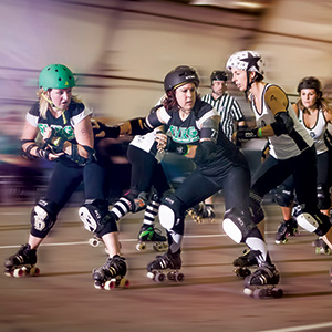 Roller derby players in helmets and protective gear compete energetically on an indoor track, with referees and spectators visible in the background.
