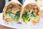 A close-up of a sliced wrap sandwich on a white plate, showing layers of lettuce, grilled meat, and other fresh vegetables inside a tortilla.
