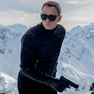 A man wearing sunglasses, black gloves, and a dark jacket holds a handgun while standing in a snowy mountain landscape under a cloudy sky.