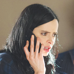 A woman with long dark hair holds a phone to her ear and looks concerned or upset as she listens during a conversation.
