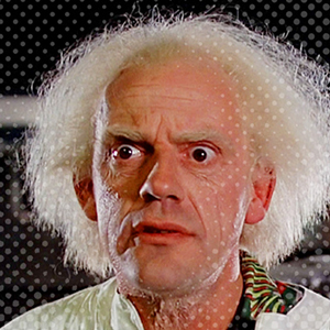 An older man with wild white hair and a surprised expression, wearing a light-colored coat. The background is dark with some blurred elements.