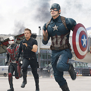 Three superheroes, including one in a red and black suit, one with a bow, and one in a blue suit with a star shield, run forward on an airport tarmac with smoke billowing in the background.