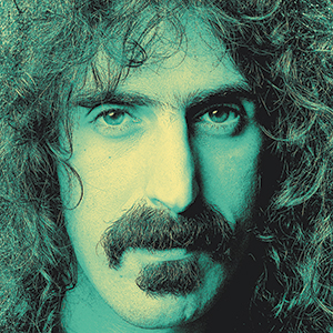 A close-up portrait of a man with long curly hair, a thick mustache, and intense eyes. The image has a greenish tint and focuses on the mans face, capturing his serious expression.