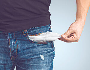 A person wearing blue jeans and a black shirt pulls out an empty pocket, suggesting they have no money.