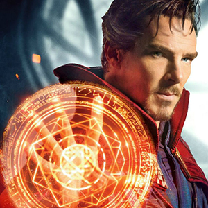 A man with a goatee and wavy hair, wearing a red cloak, holds up a glowing orange magical shield with intricate patterns in front of him. The background is blurred and dark.