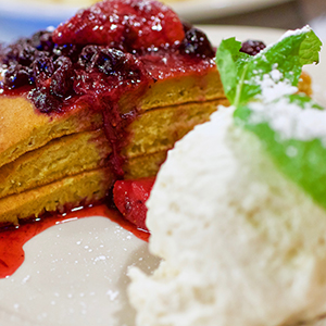 A slice of layered cake topped with berry compote sits next to a scoop of vanilla ice cream, garnished with a sprig of mint and a dusting of powdered sugar.