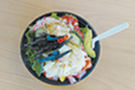 A bowl of salad with lettuce, cucumbers, tomatoes, seaweed, sliced avocado, and a fried egg on top, with a plastic fork resting on the side, viewed from above.