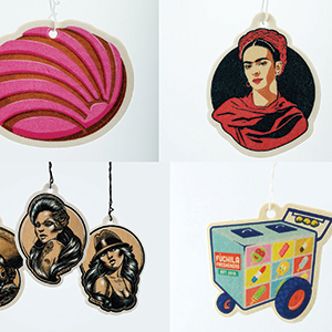 Four illustrated air fresheners: a pink shell, a portrait of Frida Kahlo, two women with vintage hairstyles, and a colorful Mexican lottery cart. Each has a string for hanging.