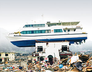 A large boat is stranded on top of a damaged building amid debris and destruction, likely after a natural disaster such as a tsunami or flood.