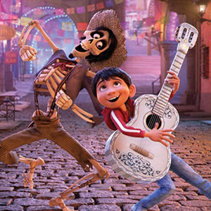 A cheerful boy plays a white guitar while standing beside a smiling skeleton in a hat on a colorful, cobblestone street with festive lights in the background.