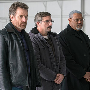 Three men stand side by side indoors, all wearing coats. The man on the left has a beard and wears a black leather jacket, the middle man has glasses and a mustache, and the man on the right has gray hair and a beard.