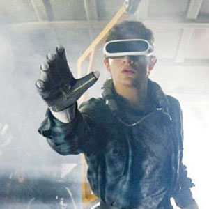 A young man wearing virtual reality goggles and a glove extends his arm forward, as if interacting with something in a digital environment. The background appears misty and industrial.
