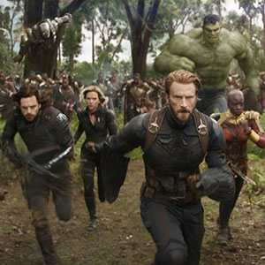 Several Marvel superheroes, including Captain America, Black Panther, Hulk, and Black Widow, charge forward through a forest with other heroes running behind them in an action scene from a movie.